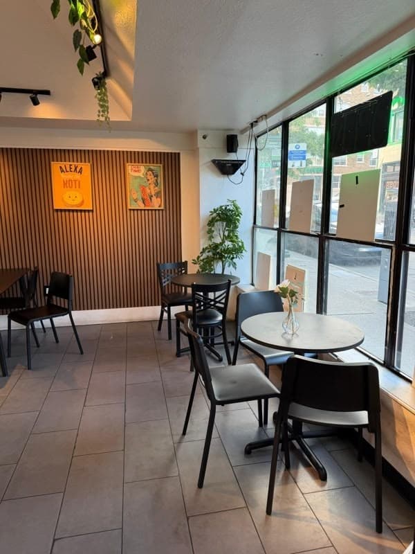 Corner seating area with round tables, wood-slat wall and framed prints beside the window wall